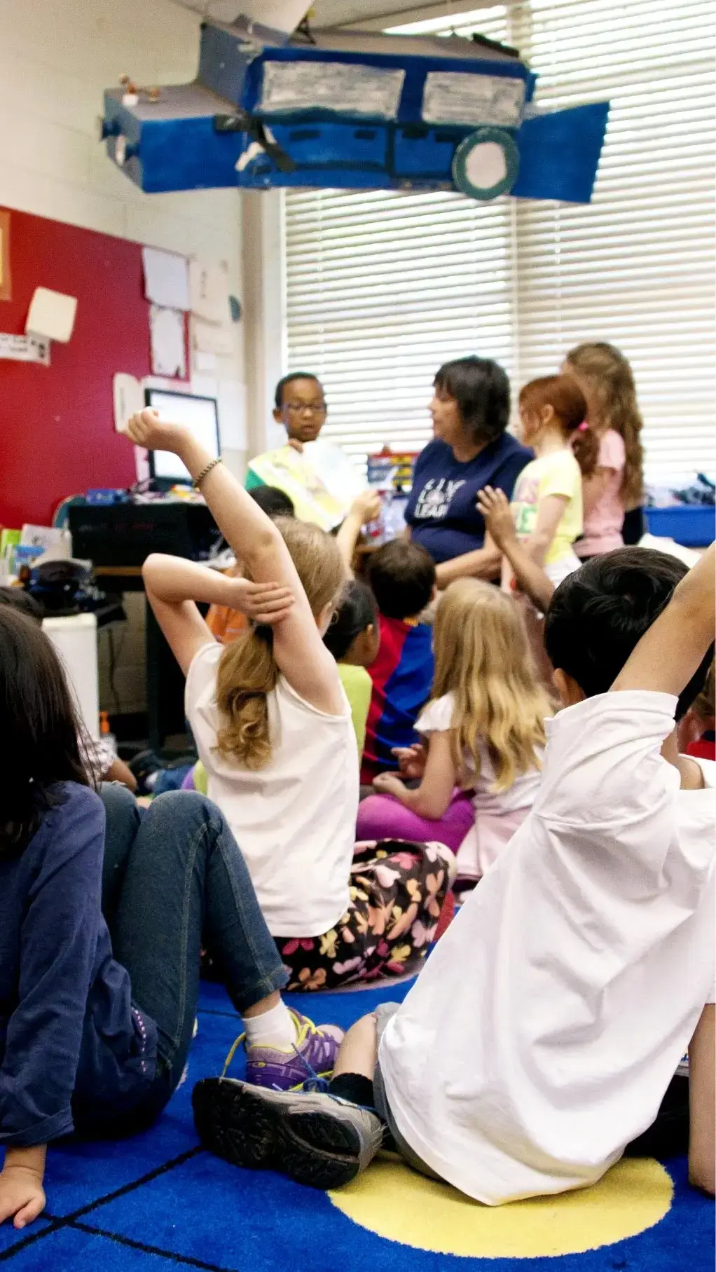 Think Small classroom scene with young children raising their hands during an early learning activity with a teacher.