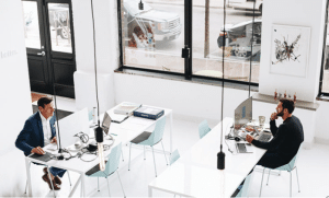 two men sitting in a white office at their desks in an urban environment handling the agency reviews